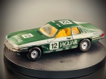 Miniatura Jaguar XJS TWR (Competing / Racing)  Corgi, Jaguar XJS em versão de competição com preparação TWR (Tom Walkinshaw Racing), ostentando o icónico verde britânico de corrida (British Racing Green), dorsal n.º 12, faixas laterais brancas e os patrocínios oficiais da época (incluindo Motul, Dunlop, Recaro, Bilstein e Champion).   Fabricante: Corgi (Made in GT. Britain, gravado na base). Med. 04x13x05 cm. Marcas do tempo e de uso.
