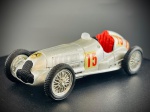 Miniatura Mercedes-Benz de Corrida Clássica  Brumm (Escala 1:43), Carro de corrida clássico Mercedes-Benz "Silver Arrow" (Flecha Prateada), em tom prateado metalizado, com o número de corrida "15" aplicado nas laterais e na traseira, detalhes gráficos históricos, grelha frontal preta com o emblema da marca, cockpit aberto com interior detalhado em vermelho e assento texturizado, para-brisas em acrílico e tubo de escape cromado exposto na lateral. Marcas do tempo e de uso.