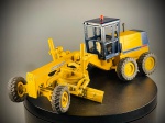 Miniatura de Motoniveladora / Máquina de Terraplanagem, escala 1:50. Motoniveladora industrial em tons de amarelo e azul, com cabine fechada azul equipada com farolim rotativo superior, lâmina central de nivelamento ajustável, eixo dianteiro direcional e conjunto de rodas traseiras duplas com pneus sulcados em borracha. "SUPERMIN", a referência "ARPRA" "MADE IN BRAZIL", complementada com inscrições e logótipos decorativos da marca "KOMATSU". Marcas do tempo e de uso. Marcas do tempo e de uso.