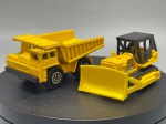 Miniaturas de Construção Civil e Obras  Matchbox Lesney (Made in England) / Escala 1:43, par de veículos industriais e de construção civil da prestigiada marca britânica Matchbox (Série Lesney). O lote é composto por um camião basculante pesado de grande capacidade de carga e por um trator de rastos equipado com lâmina frontal e cabina aberta em tom escuro. Marcas do tempo e de uso.