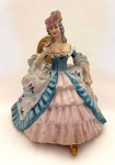 Escultura de coleção representando dama de época, sentada segurando flor, em biscuit, em perfeito estado. Med. 19x16x13 cm.