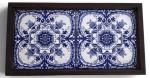 Bandeja retangular em madeira nobre, com fundo composto por dois azulejos decorativos em tons de azul e branco, de inspiração portuguesa, com motivos florais. Peça elegante e funcional, ideal para servir ou decorar ambientes clássicos e coloniais. Mede 17x33cm.