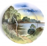Prato decorativo em porcelana, pintado à mão, representando paisagem lacustre com árvores, vegetação e céu em suaves tonalidades. Peça de caráter artístico, ideal para decoração de parede ou composição em coleção de porcelanas pintadas à mão. Mede 20cm de diâmetro.