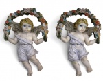 Par de anjos decorativos confeccionados em resina policromada, representando querubins alados sustentando guirlandas florais. Peças ricamente detalhadas, próprias para decoração de parede, com argolas metálicas para fixação. Mede 12x17cm.