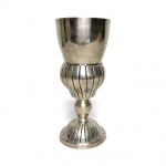 Cálice litúrgico antigo em metal espessurado a prata, corpo almofadado com sulcos verticais e base modelada em gomos. Peça de presença, elegante e com pátina natural do tempo. Ideal para composições decorativas ou acervo sacro. Possui registro na base. Mede 25 cm.