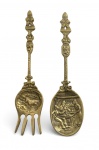 Conjunto de colher e garfo decorativos em bronze dourado, origem holandesa, com rica decoração em relevo. Cabos trabalhados com motivos heráldicos e cenas figurativas, conchas ilustradas com temática campestre e interior doméstico, com inscrições VOLENDAM e HOLLAND. Peças de caráter decorativo e colecionável, com pátina original do tempo. Mede 23 cm.