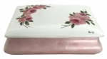 Caixa decorativa em porcelana esmaltada, formato retangular, com tampa. Decoração floral pintada à mão, com rosas em tons de rosa e folhas verdes sobre fundo branco. Corpo externo em tom rosado fosco e interior esmaltado claro. Peça de acabamento delicado, ideal para uso decorativo ou guarda de pequenos objetos. Em bom estado de conservação. Mede 19cm x 14cm.
