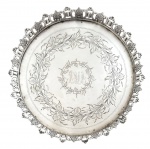 PRATA DE LEI DO PORTO - Elegante salva de prata portuguesa, de formato circular, com rica decoração gravada em motivos florais e guirlandas, apresentando monograma central. Borda recortada e vazada com acabamento trabalhado, apoiada sobre pés. Verso com marcas de contraste indicando teor de prata 833 milésimos e provável origem no Porto. Peça de apelo clássico, ideal para composição de mesa ou decoração refinada. Peso 560 g. Mede 22,5 cm.