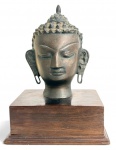 Antiga escultura em bronze representando cabeça de Buda, com rica textura capilar e expressão serena, montada sobre base retangular em madeira nobre. Peça de caráter decorativo, inspirada na estatuária oriental. Ideal para decoradores e colecionadores. Mede 20 x 13,5 cm.