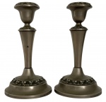 Par de castiçais em metal espessado a prata, fabricação inglesa, marca IANTHE, conforme inscrição Silver Plated  Made in England na base. Modelo de linhas elegantes com corpo afunilado e decoração em relevo floral nas bordas, típico do gosto clássico do século XX. Apresenta sinais do tempo e uso, com desgastes e oxidação interna. Mede 18cm de altura.