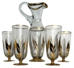 Conjunto em vidro artístico translucido, composto por jarra e quatro copos, decorados com motivos florais estilizados em dourado e negro, com detalhes aplicados à mão e bordas douradas. Peças com elegante influência Art Déco, apresentando bases metálicas douradas. Medida do maior 33cm de altura.