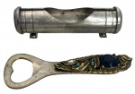 Abridor de garrafas em metal prateado, acompanhado de suporte tubular metálico. Cabo com aplicação decorativa em relevo vegetal e pedra azul em estilo modernista. Sinais de uso e oxidação do tempo. Medida do maior 11cm.