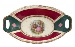 ALEMANHA SÉC. XIX - Travessa em porcelana alemã Bavaria Waldershof, modelo nº 5633, formato oval com alças laterais vazadas. Decoração policromada com bordas em tons de verde e vinho, detalhes dourado vibrante e cena galante central em estilo clássico. Marca na base Made in Germany. Meados séc. XX. Mede 33,5 x 19 cm.