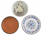Conjunto composto por três pratos decorativos, incluindo exemplar em porcelana com decoração floral policromada, prato em tom âmbar de acabamento esmaltado e prato com pintura floral em relevo sobre fundo acetinado. Peças de diferentes origens e épocas, ideais para composição decorativa ou coleção.Maior medida: 25 cm de diâmetro.