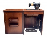 SINGER  Máquina de costura antiga com gabinete em madeira, apresentando ferragens e detalhes originais, compartimentos laterais e pedal mecânico. Marca SINGER identificada na máquina e no emblema. Peça de caráter vintage, com marcas do tempo e sinais de uso.Medidas: 76 cm de altura x 114 cm de comprimento aberta x 42 cm de profundidade; fechada, 57 cm de comprimento.