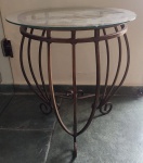 Mesa de canto com estrutura em ferro na tonalidade dourada envelhecida com tampo em vidro. Obs: Dois bicados no tampo. RETIRADA PELO COMPRADOR. Medida: altura 55 cm diâmetro 47 cm. 