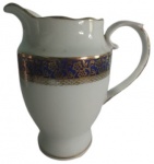 REAL - Leiteira em porcelana branca pintado artesanalmente com guirlandas na tonalidade dourado e fundo azul. Medidas: 15 cm de altura, 10 cm de largura e 15 cm de comprimento.