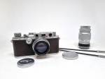 Câmera Leica DRP Ernst Leitz Wetzlar (número de série 215010). Acompanham 2 lentes: Summitar f=5cm 1:2 e Elmar f=9cm 1:4. Em ótimo estado de conservação. Lentes sem fungos. Acompanha disparador duplo Leitz (não necessariamente para a câmera aqui oferecida). Sem garantia de funcionamento. Coleção Carlos Frederico Cardoso, Rio de Janeiro/RJ.