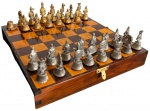 Jogo de xadrez de inspiração oriental, possivelmente indiana, composto por tabuleiro dobrável em madeira, formando estojo com compartimentos individuais para acondicionamento das peças. Conjunto com peças figurativas em metal, em dois acabamentos, dourado e prateado, ricamente trabalhadas. Medidas: caixa fechada: 11 x 21,7 x 6,8 cm; tabuleiro aberto: 22 x 21,7 x 3,4 cm. Apresenta marcas do tempo e de uso faltar uma peça.