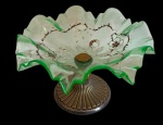 Antiga fruteira de mesa em vidro, com bojo amplo de borda ondulada e recortada, realçada em tonalidade verde, apresentando delicada decoração floral. Apoiada sobre base circular em metal, trabalhada com decoração canelada em relevo, apresentando sinais compatíveis com o tempo e uso. Medidas: 20 x 32 cm de diâmetro.