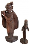 Duas esculturas em madeira entalhada, representando figuras distintas tradições culturais. A maior, de inspiração oriental, apresenta figura feminina com vestes e ornamentos entalhados, carregando recipiente às costas; a menor representa figura masculina estilizada. Medidas: 20 x 7 x 3 cm e 12,5 x 5 x 4,5 cm.