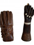 Duas esculturas decorativas em madeira entalhada, sendo uma representando cabeça masculinae outra uma figa, com aplicações nas unhas e bracelete em metal com decoração em relevo. Medidas: 14,5 x 7 x 6 cm e 18 x 5 cm.