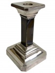 Antigo castiçal de mesa, em metal prateado, com coluna central de seção quadrangular e base escalonada. Apresenta contraste/marca de manufatura na base. Medidas: 20 x 12 x 12 cm.
