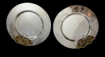 Par de bandejas circulares em metal espessurado a prata, com centro liso e abas largas, guarnecidas por alças ornamentais em metal dourado, executadas em forma de cordão torcido, Apresentam sinais e desgastes compatíveis com o tempo de uso. Medidas: 31 x 3 cm cada.