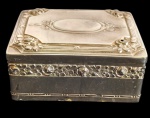 Antiga caixa porta-joias em metal espessurado a prata, de formato retangular, ricamente ornamentada em relevo com motivos florais e rosáceas, apresentando tampa decorada com medalhão oval central e frisos geométricos. Laterais guarnecidas por faixa vazada com flores e folhagens em relevo. Medidas: 10 x 4,5 x 8 cm.