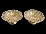 Par de pequenas fruteiras em metal espessurado a prata, de formato circular, com corpo ricamente trabalhado em relevo, apresentando motivos florais e volutas, bordas recortadas e base circular elevada. Medidas: 6 x 14 cm de diâmetro.