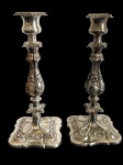 Par de antigos castiçais em metal espessurado a prata, de elegante inspiração barroca, ricamente trabalhados em relevo com motivos florais, folhagens e volutas. Fustes torneados e ornamentados, apoiados sobre bases quadrangulares recortadas com rica decoração em relevo. Medidas: 30 x 13,6 x 13,6 cm.