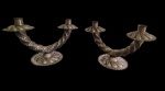 Antigo par de castiçais duplos em metal, de formato curvilíneo, com braços retorcidos e ornamentação relevada, bases e arandelas recortadas com motivos florais. Para duas velas cada. Apresentam marcas do tempo e desgaste da superfície. Medidas: 24,5 x 24 x 17,5 cm.