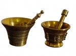 Dois antigos pilões em bronze, ambos acompanhados de respectivos socadores, apresentando formatos distintos, sendo um de corpo cônico com frisos horizontais e outro com ornamentação em relevo. Apresentam pátina e marcas do tempo. Medidas: 6,7 x 8 x 5 cm e 4,5 x 6 cm.
