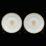 ROSENTHAL SELB BAVARIA. Par de pratos decorativos em fina porcelana alemã branca, ornamentados ao centro com brasão de armas em douração, composto por escudo heráldico encimado por coroa e elmo, ladeado por rica composição floral e arabescos, evocando insígnias de nobreza e tradição aristocrática europeia. As bordas apresentam delicado friso trançado em ouro.Manufatura no verso. Medidas: 19,5 cm de diâmetro