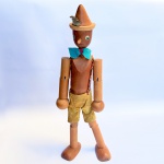 Antigo boneco em madeira articulada representando o clássico personagem Pinóquio, roupa em camurça. Med 50 cm.