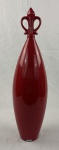MAZZOTTI. Vaso decorativo em cerâmica vermelha com corpo alongado e ornamento superior em forma de flor-de-lis. Etiqueta na base. Medindo: 57 x 12 cm.