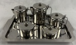 Aparelho para servir café e chá, confeccionado em aço inox, constando: 1 Bule para café, 1 bule para chá, 1 cremeira, 1 açucareiro, 1 manteigueira e 1 bandeja. Sem uso em estojo original.