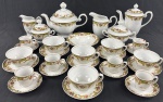 REAL. Conjunto para chá e café em porcelana nacional, esmlatada na cor branca, bordas com ondulações, delicadamente decorada com flores policrima, guirlandas e frisos dourados composto de bule de café (19 x 18 cm.), bule para chá (20 x 24 cm.), açucareiro (13 x 15 cm.), leiteira (11 x 11 cm.), chocolateira (12cm.), cremeira (10cm.), manteigueira  sem tampa (10cm), porta-geléia (3,5 x 15,5cm.), 6 xícaras para café e 6 xicaras para chá com respectivos pires. Suaves sinais de uso, bule com bicado no bico, açucareiro com bicado na borda e uma xícara de café bicada.