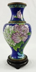 Vaso chinês em metal esmaltado de cloisonné, com fundo azul-cobalto e rica decoração policromada de flores, folhagens e motivos orientais. Acompanha peanha em madeira entalhada e vazada. Medidas: vaso: 26 cm de altura; peanha: 4 x 11 cm.