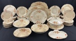 ALFRED MEAKIN ENGLAND, modelo Marigold, formato Astoria, padrão Hillingdon. Serviço de jantar em faiança inglesa, decorado com motivos florais policromados e filetes dourados, composto por 67 peças: 18 pratos rasos, 12 fundos, 26 de sobremesa, sopeira, 3 saladeiras, 2 pratos para bolo, bandejinha e 4 travessas. Medidas: pratos: 23 cm, 3,5 x 23 cm e 18 cm de diâmetro; sopeira: 14 x 27 cm; saladeiras: 8 x 26 cm, 6 x 24 x 19 cm e 7 x 26 x 21 cm; pratos para bolo: 28 cm e 26 x 28 cm; bandejinha: 19 x 25 cm; travessas: de 21 x 27 cm a 31 x 37 cm. Apresentam manchas e alguns com craquelê. 1 prato raso e 1 saladeira oval com fio de cabelo; 3 pratos de sobremesa com bicados e fios de cabelo; 1 travessa com batida seca e fio de cabelo.