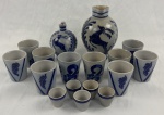 Conjunto para vinho em cerâmica vitrificada, na tonalidade cinza, com decoração em azul-cobalto de motivos estilizados e cervos em relevo, composto por 17 peças: 2 jarras, 4 copos, 6 copos com decoração distinta e 5 copinhos para shot. Medidas: jarras: 22 x 16 x 13 cm e 15 x 12 x 11 cm; copos: 9 x 7,5 cm; copinhos para shot: 4,5 x 4,5 cm.