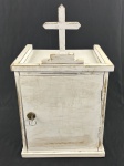 Oratório/sacrário de formato cúbico, encimado por cruz latina em madeira entalhada e fixada sobre base escalonada no topo. Possui porta única com dobradiças embutidas. O interior  forrado em tecido acolchoado, fechadura em metal cromado do tipo tambor com a chave inclusa. Obs.: Necessita de repintura. Medindo: 54 x 32 x 31 cm