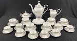 SCHMIDT, Santa Catarina. Serviço de chá e café em porcelana branca esmaltada, com decoração floral policromada, detalhes moldados em relevo e filetes prateados, composto por: bule com tampa, leiteira, açucareiro, manteigueira, 6 xícaras de chá com respectivos pires e 8 xícaras de café com respectivos pires. Medidas: bule: 30 x 28 x 15 cm; leiteira: 16 x 16 cm; açucareiro: 14 x 18 cm; manteigueira: 4 x 16,5 cm. Uma xícara de café apresenta fio de cabelo.