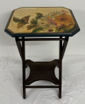 Mesa lateral em madeira, com tampo octogonal pintado à mão, decorado com composição floral em policromia e assinado, contornado por frisos dourados e moldura verde. Estrutura com pés levemente arqueados, travessas e prateleira inferior recortada. Apresenta marcas do tempo e desgastes na pintura. Medidas: 55 x 35 x 40 cm.