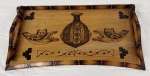 Bandeja em madeira tipo bambu, com laterais curvas e alças recortadas, decorada por meio de pirografia com motivos geométricos, vaso e máscaras de inspiração africana. Verso com padrão reticulado e pequenos pés de apoio. Medidas: 5 x 27 x 49 cm.