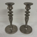 Par de castiçais em estanho, no estilo clássico com base redonda e corpo moldado. Medida: 20 cm de altura.