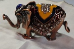 Porta-joias em metal esmaltado, em formato de elefante, com corpo articulado, ricamente ornamentado com aplicações de cristais Swarovski e esmaltação policromada nas tonalidades azul, amarelo, branco e vinho. Medidas: 5 x 12 cm.