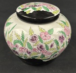 Pote bojudo com tampa em porcelana esmaltada, decorado à mão com profusa composição floral em policromia, sobre fundo branco, com reservas em esmalte preto. Assinado e datado na base. Apresenta desgaste no esmalte da tampa. Medidas: 17 x 20 cm.