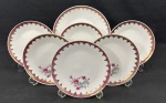 SCHMIDT, SANTA CATARINA. Conjunto em porcelana branca, composto por um prato raso e cinco pratos para sobremesa, com decoração de rosas em policromia, faixa vinho e profusos ornamentos dourados. Total: 6 peças. Marca do fabricante na base. Medidas: 25 cm e 18 cm de diâmetro. O prato para bolo apresenta fio de cabelo, e um prato para sobremesa apresenta bicado.