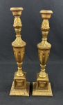 Par de altos castiçais em madeira entalhada e patinada en dourada, em estilo Neoclássico, com fustes torneados e ornamentados por folhas de acanto, reticulados e elementos vegetalistas, sobre bases quadrangulares molduradas. Apresentam marcas do tempo e desgastes na douração. Medidas: 50 x 12 cm cada.